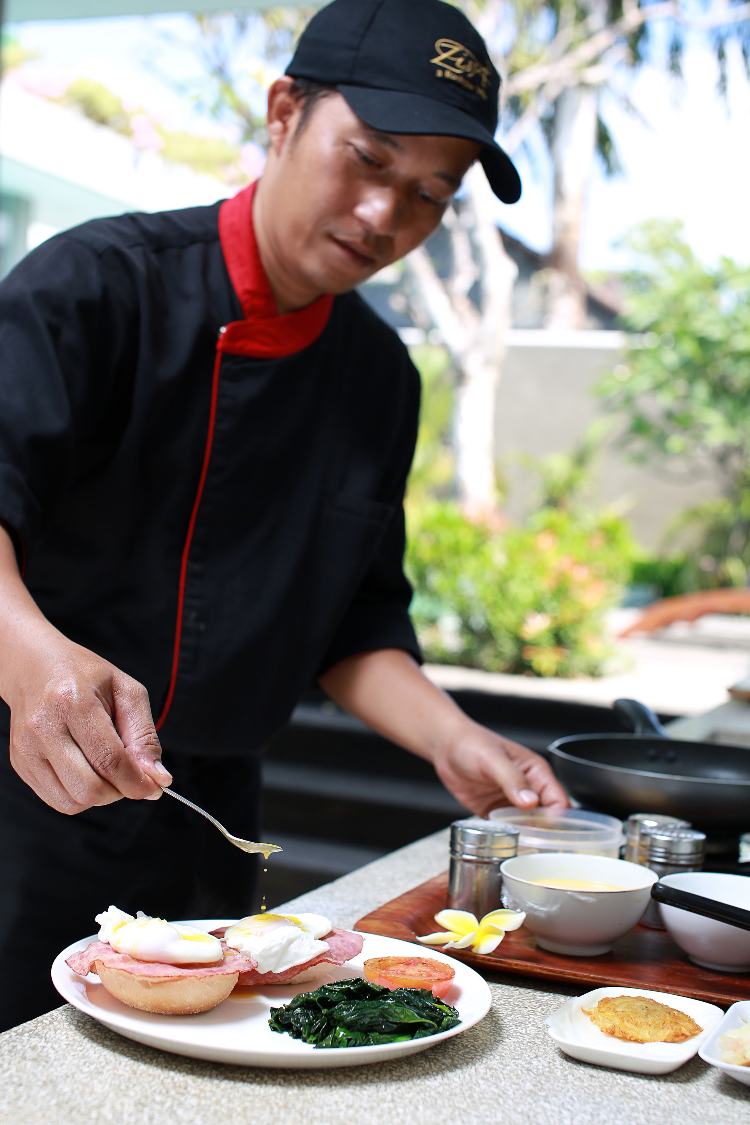 A chef preparing food with a focus on a plate with eggs, greens, and a small dish of sauce.