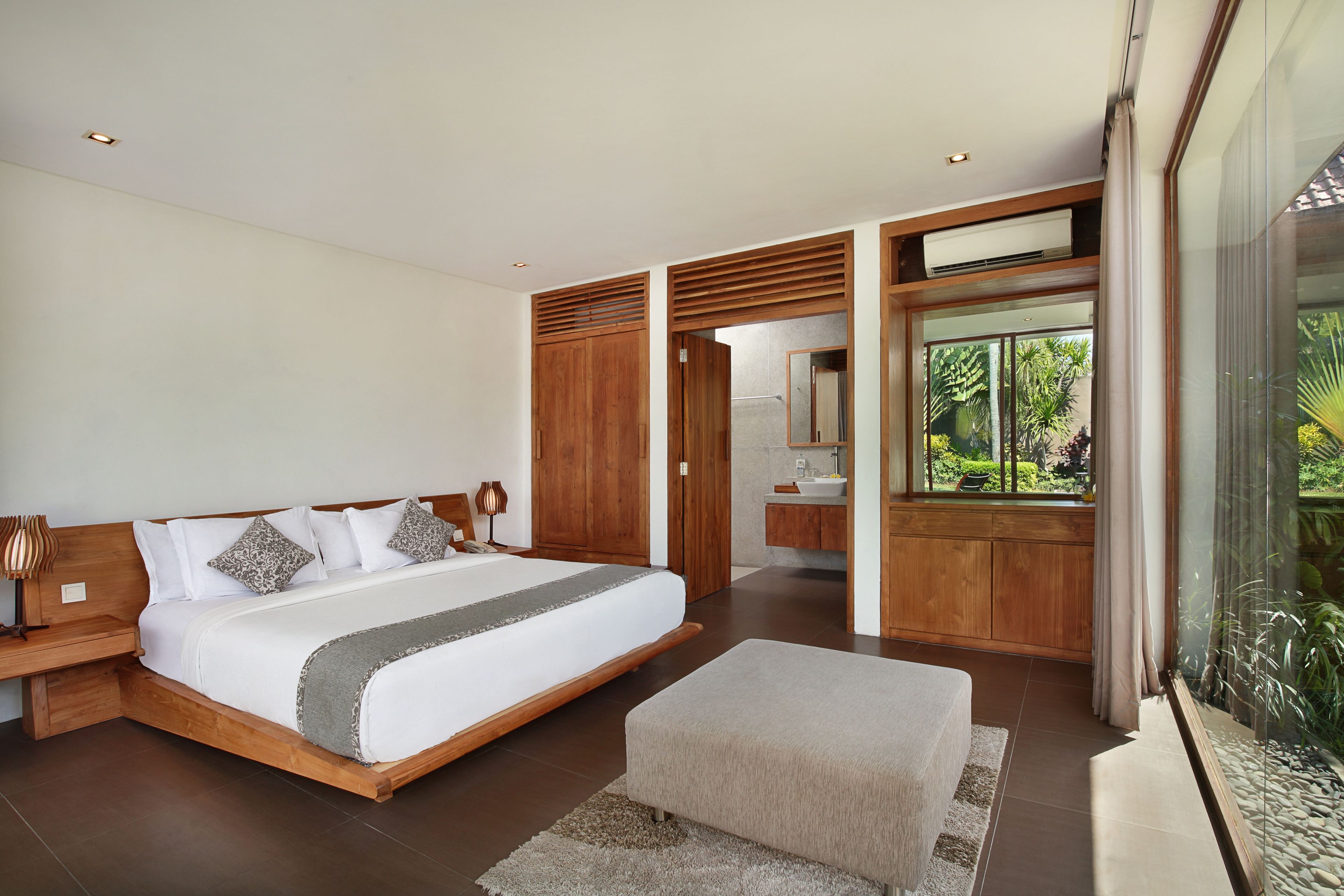 Ein modernes Schlafzimmer mit einem großen Bett, einem Holz-Kopfende und Blick auf einen üppigen Garten durch eine Glastür.