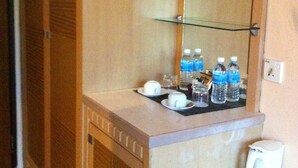 A hotel room with a wooden cabinet, a countertop with a glass shelf holding water bottles, a white electric kettle, and a mirror above the shelf. - D' Borneo Hotel (Kota Kinabalu)