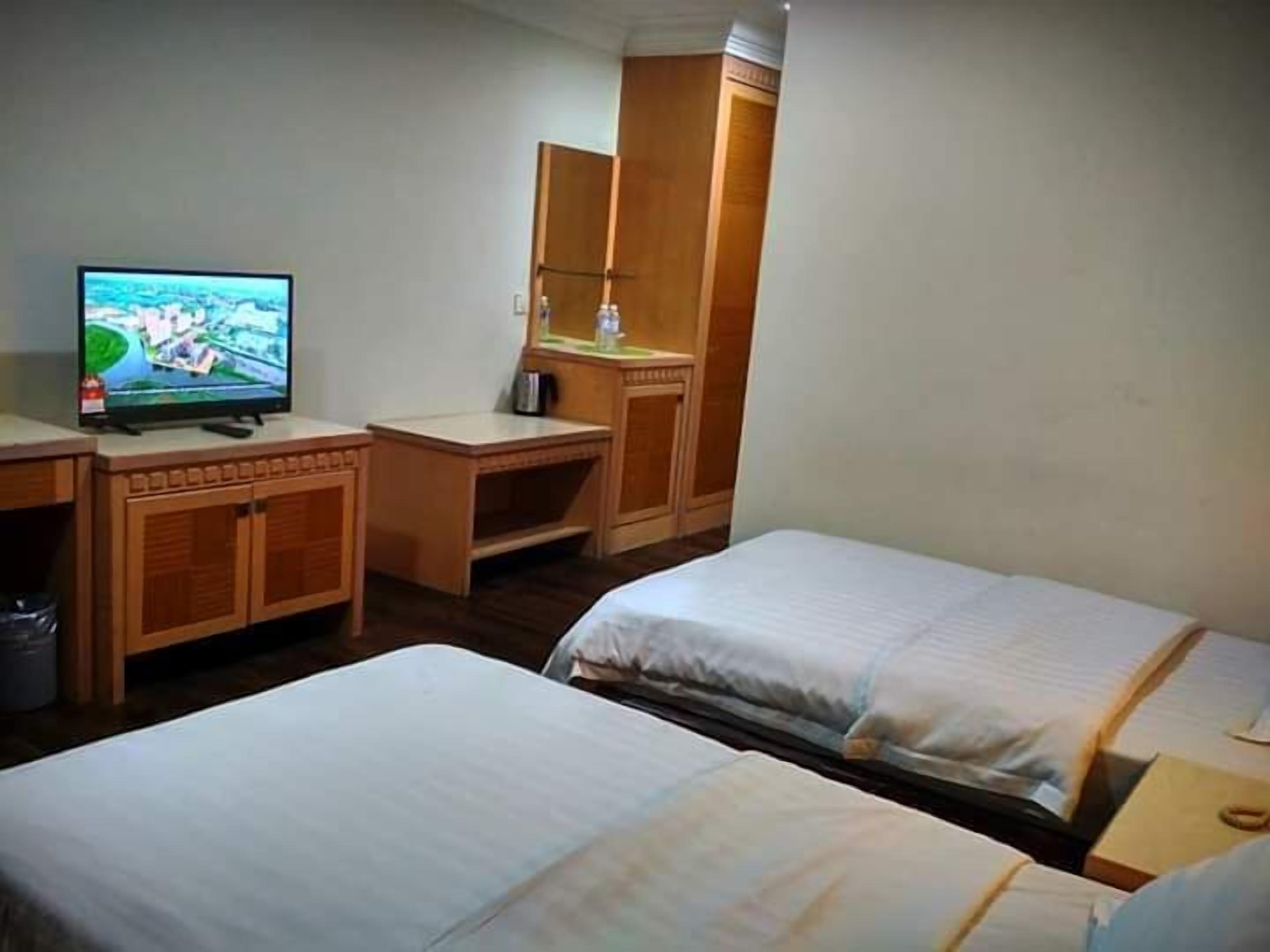 A hotel room with two beds, a desk, a television, and a wardrobe.
