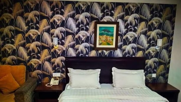 A hotel room with a patterned wallpaper, a bed with white linens, a nightstand with a telephone, and an orange chair. - D' Borneo Hotel (Kota Kinabalu)