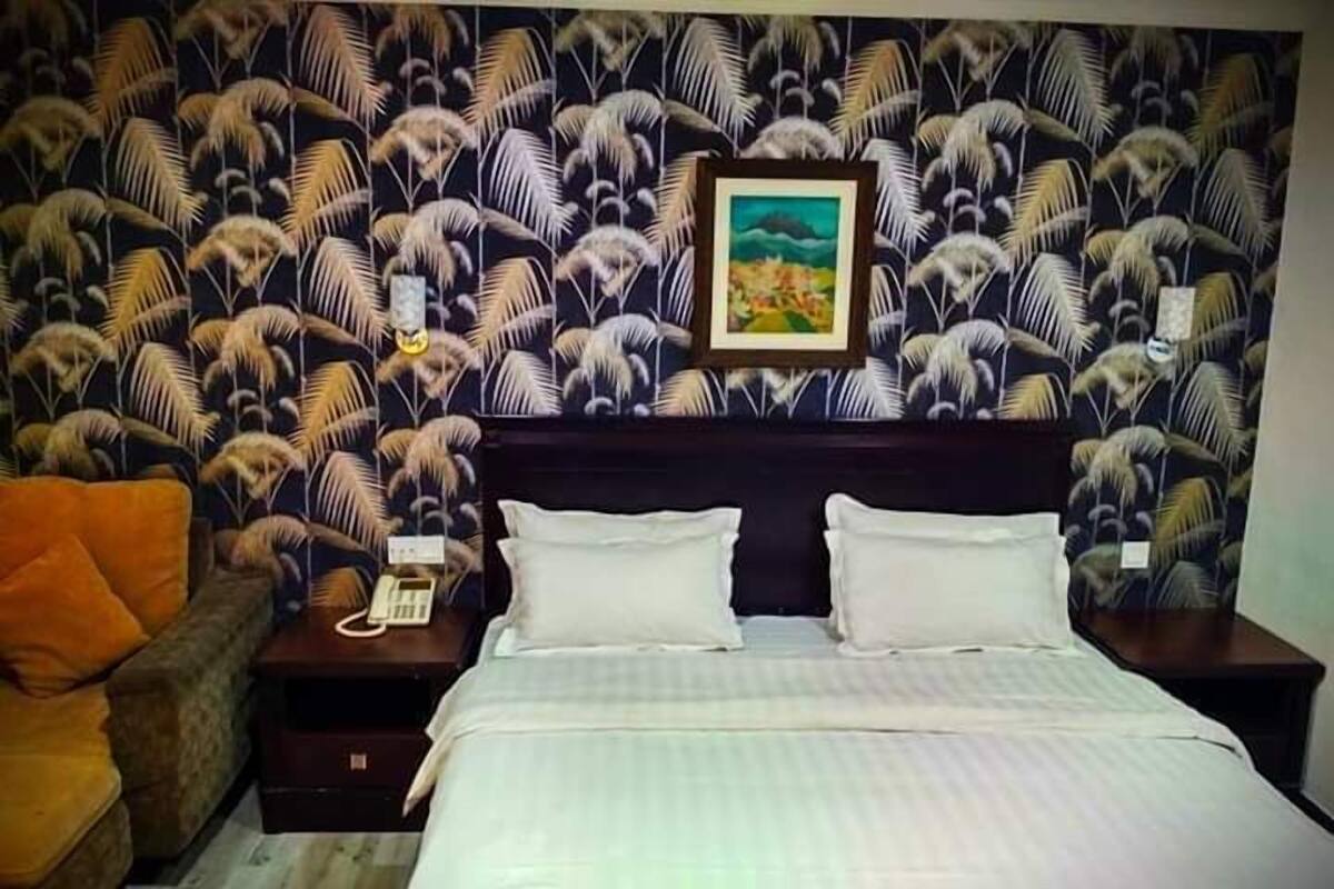 Ein Hotelzimmer mit gemustertem Wandpapier, einem Bett mit weißer Bettwäsche, einem Nachttisch mit Telefon und einem orangefarbenen Sessel.