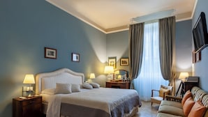A hotel room with a bed, bedside tables, a chair, a sofa, a TV, and a window with curtains. - Opera Boutique B&B (Florence)