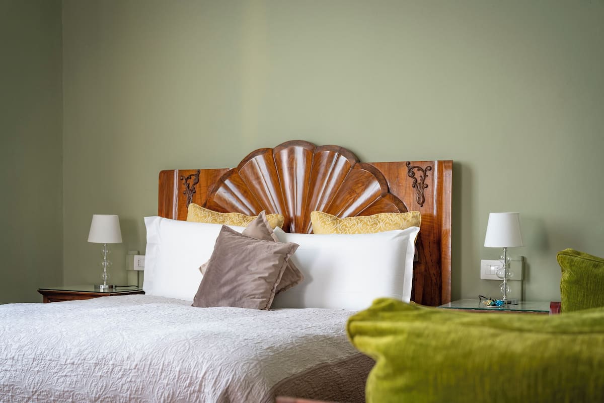 Una cama bien tendida con cabecera de madera, dos lámparas de noche y un cojín verde.