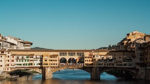 A historic bridge with multiple arches spanning a river, surrounded by traditional buildings with balconies and windows. - Opera Boutique B&B (Florence)