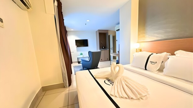 Ein Hotelzimmer mit einem ordentlich bezogenen Bett, einem an der Wand montierten Fernseher und einem Schreibtisch mit Stuhl.