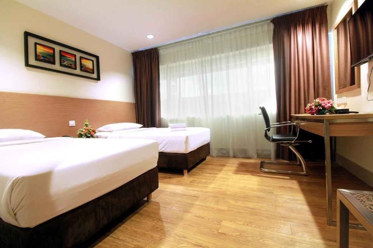 Ein Hotelzimmer mit zwei Betten, einem Schreibtisch, einem Sessel, einem Fernseher und einem Fenster mit Vorhängen.