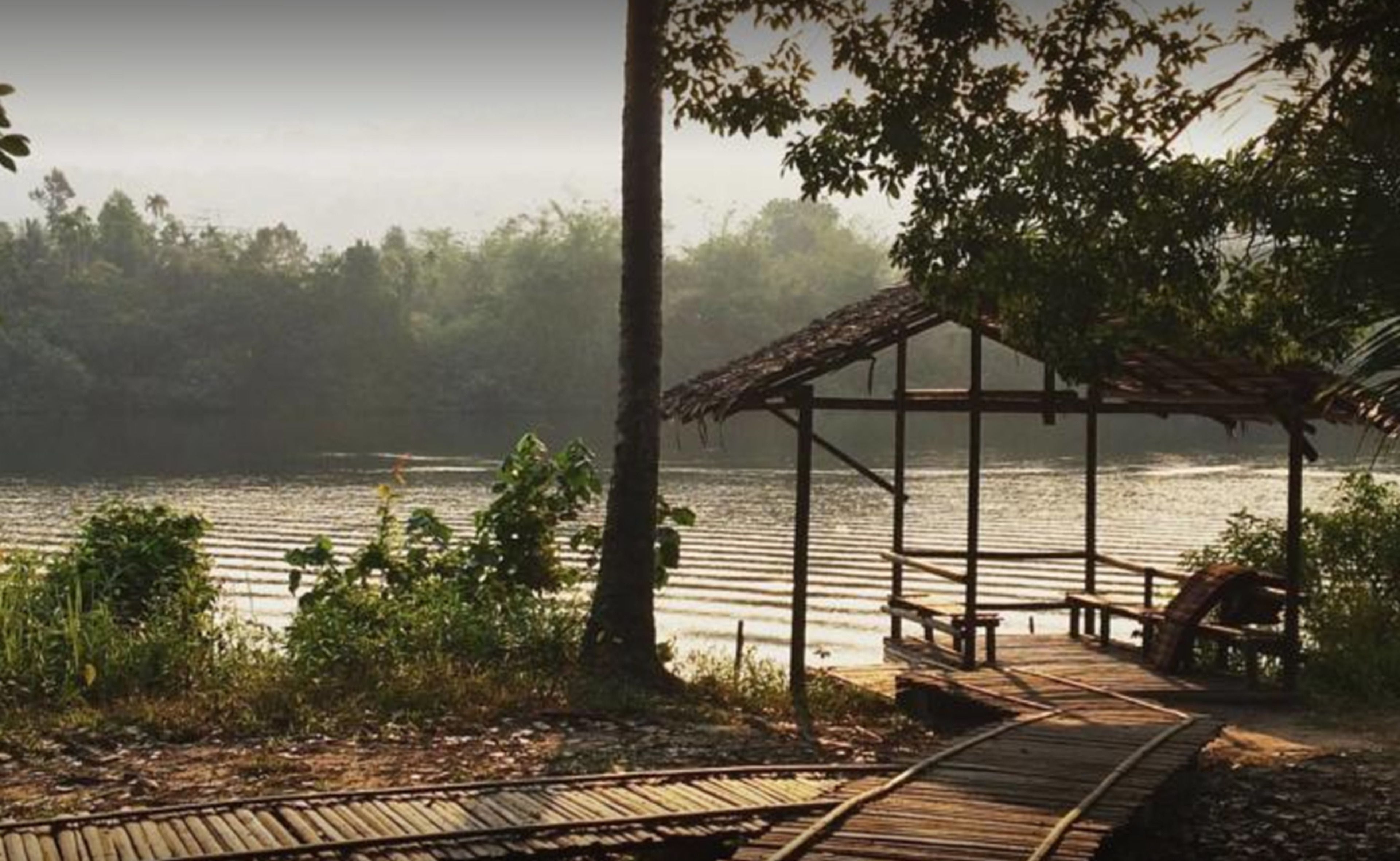 A wooden pier leading to a covered structure by a calm lake, surrounded by trees.