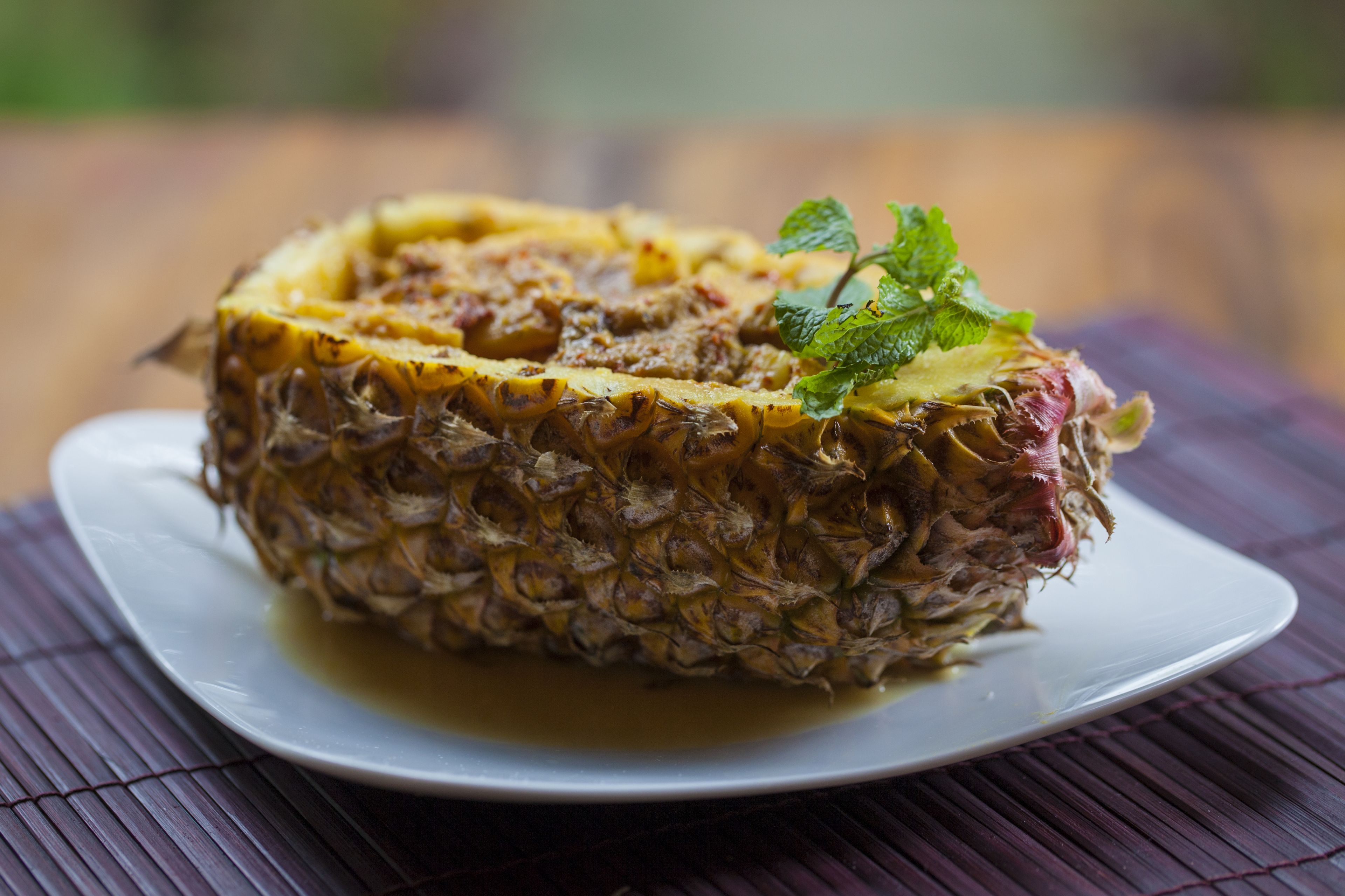 A pineapple on a white plate with a green leaf garnish, placed on a bamboo mat.