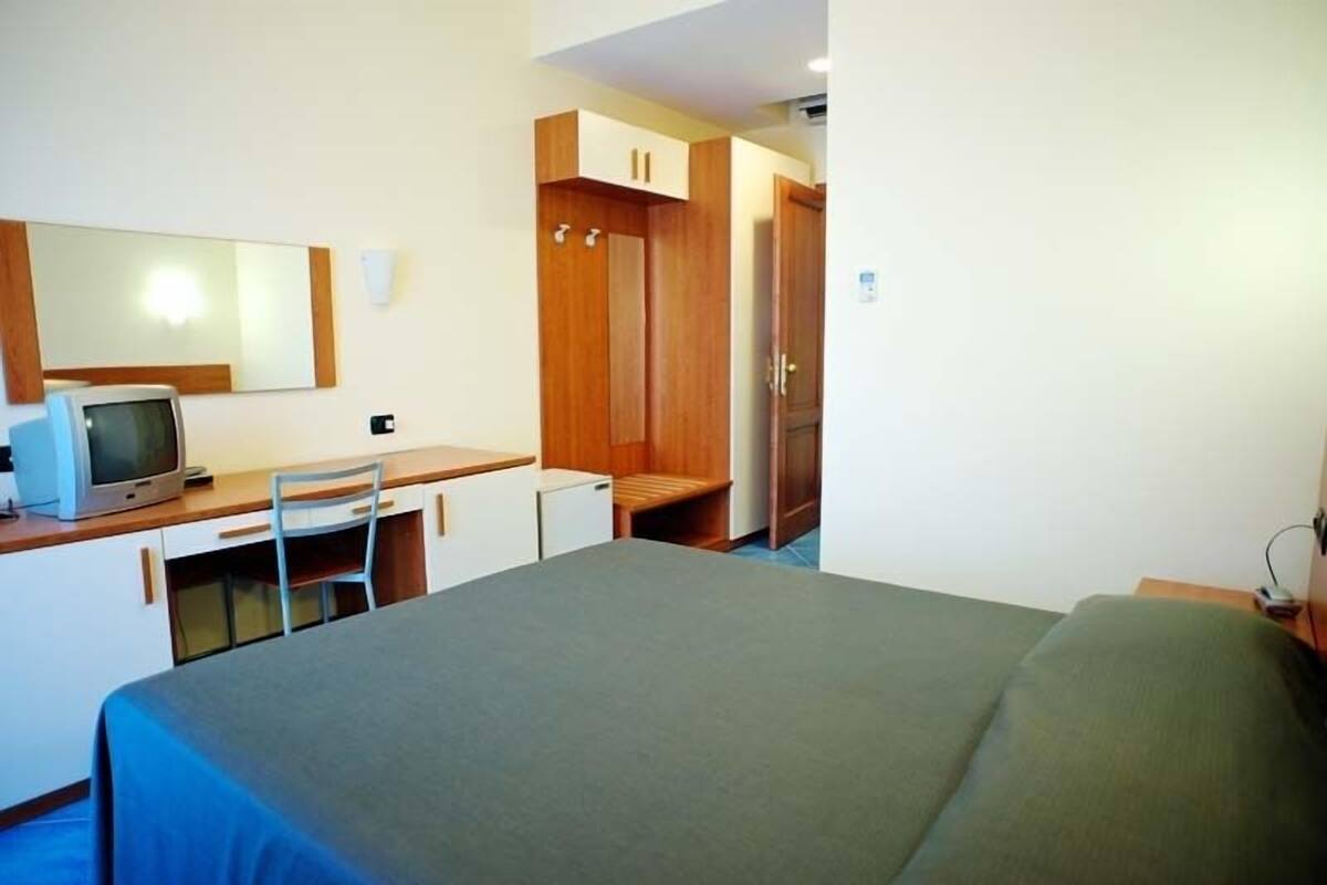 A hotel room with a bed, a desk with a chair, a television, and a wardrobe.