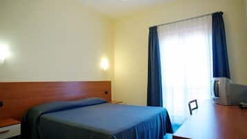Una camera d'albergo con un letto singolo, una testiera in legno, una scrivania con televisore e una finestra con tende.