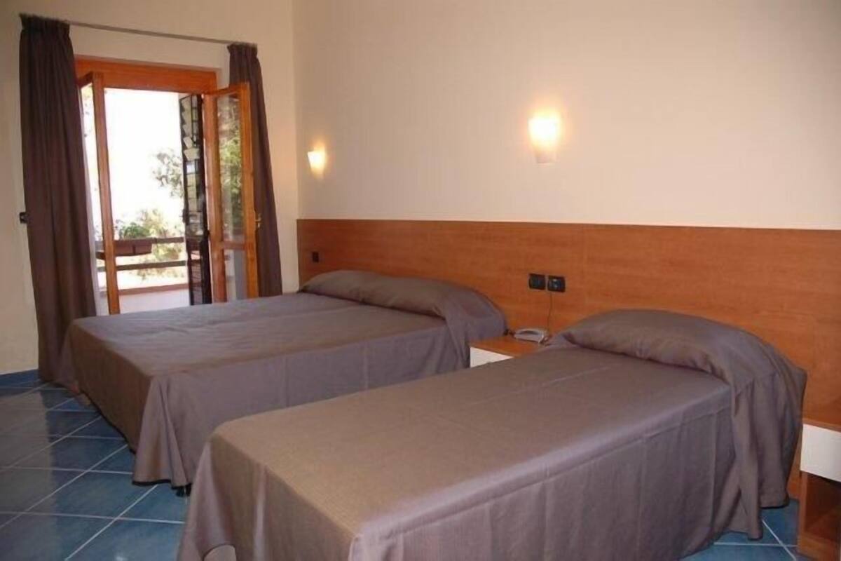 A room with two beds, a wooden headboard, a nightstand, and a door leading to an outdoor area.