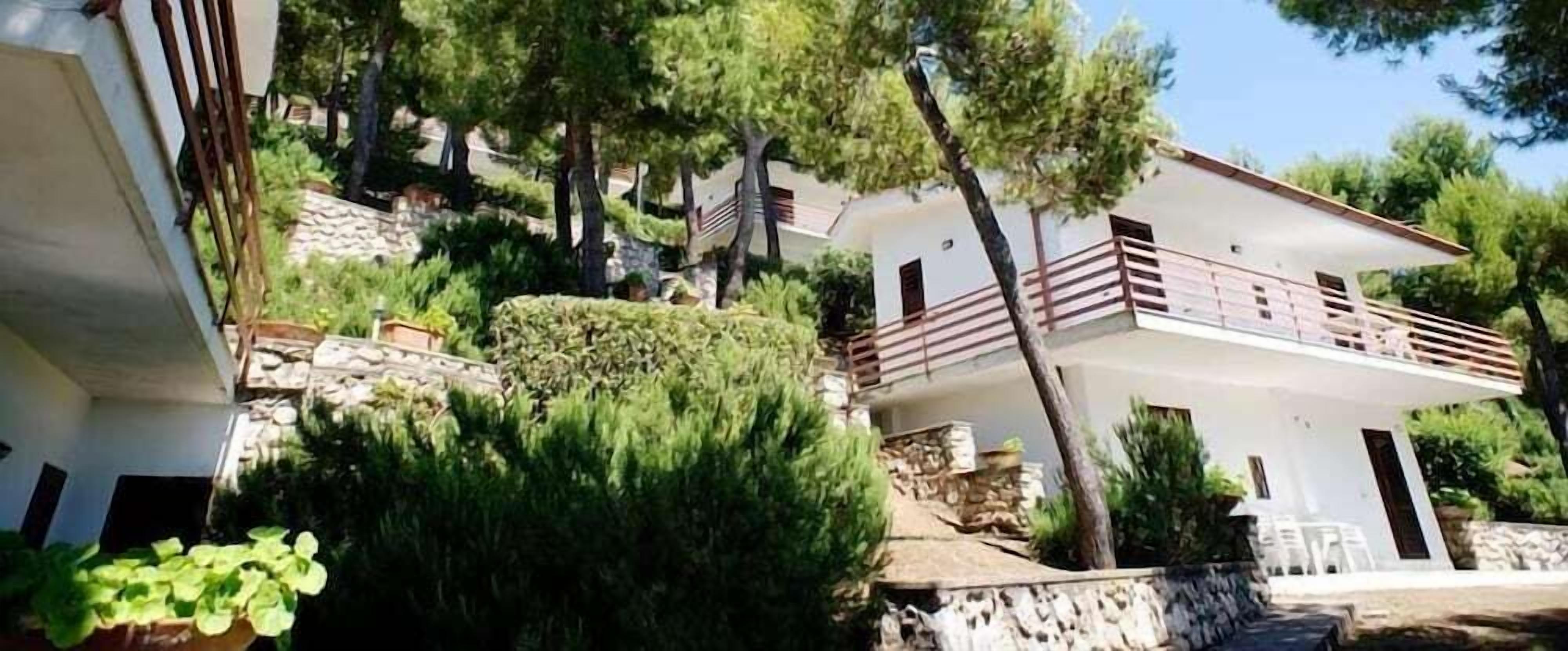 Un bâtiment à deux étages doté d’un balcon, entouré de verdure et d’arbres.
