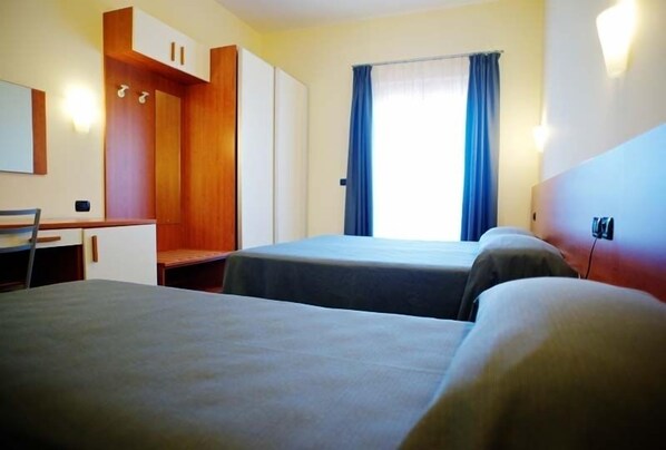 Ett hotellrum med två sängar, ett skrivbord, en garderob och ett fönster med gardiner.