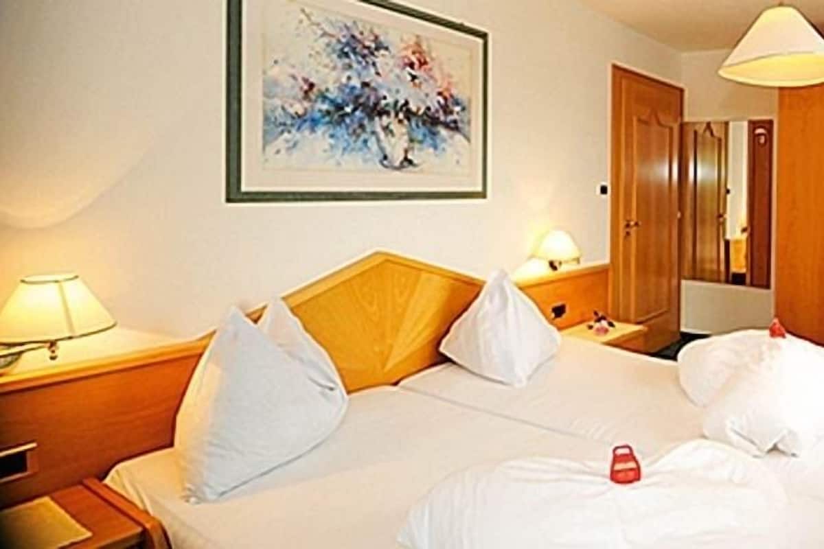 Une chambre d’hôtel avec un lit, des tables de chevet, une lampe, un tableau et une armoire.