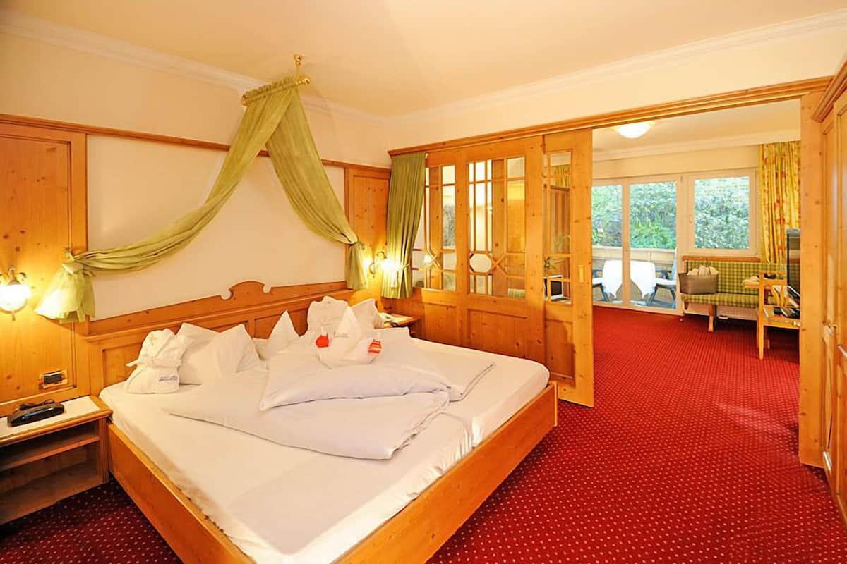 Une chambre d’hôtel avec un grand lit, une tête de lit en bois et une moquette rouge. On y trouve également une armoire en bois et une fenêtre avec des rideaux.