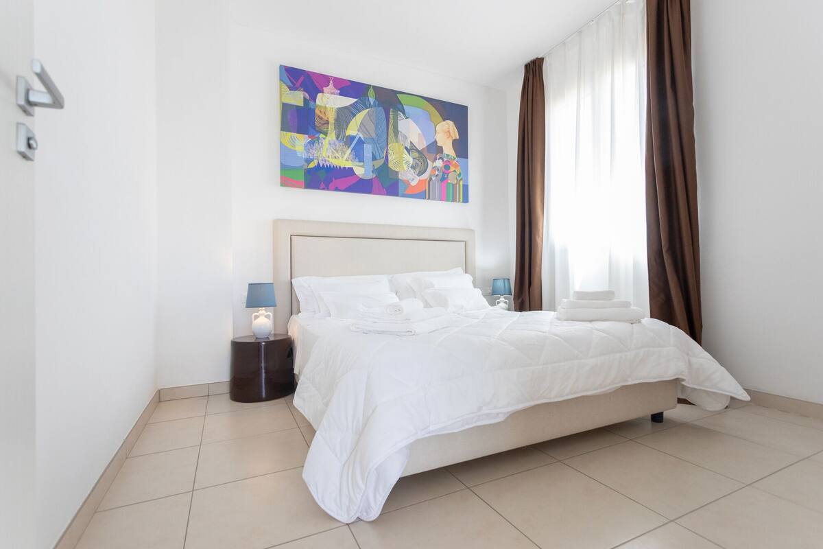 A hotel room with a bed, a nightstand, a lamp, and a painting on the wall.