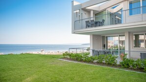 A modern two-story house with a balcony overlooking a beach.