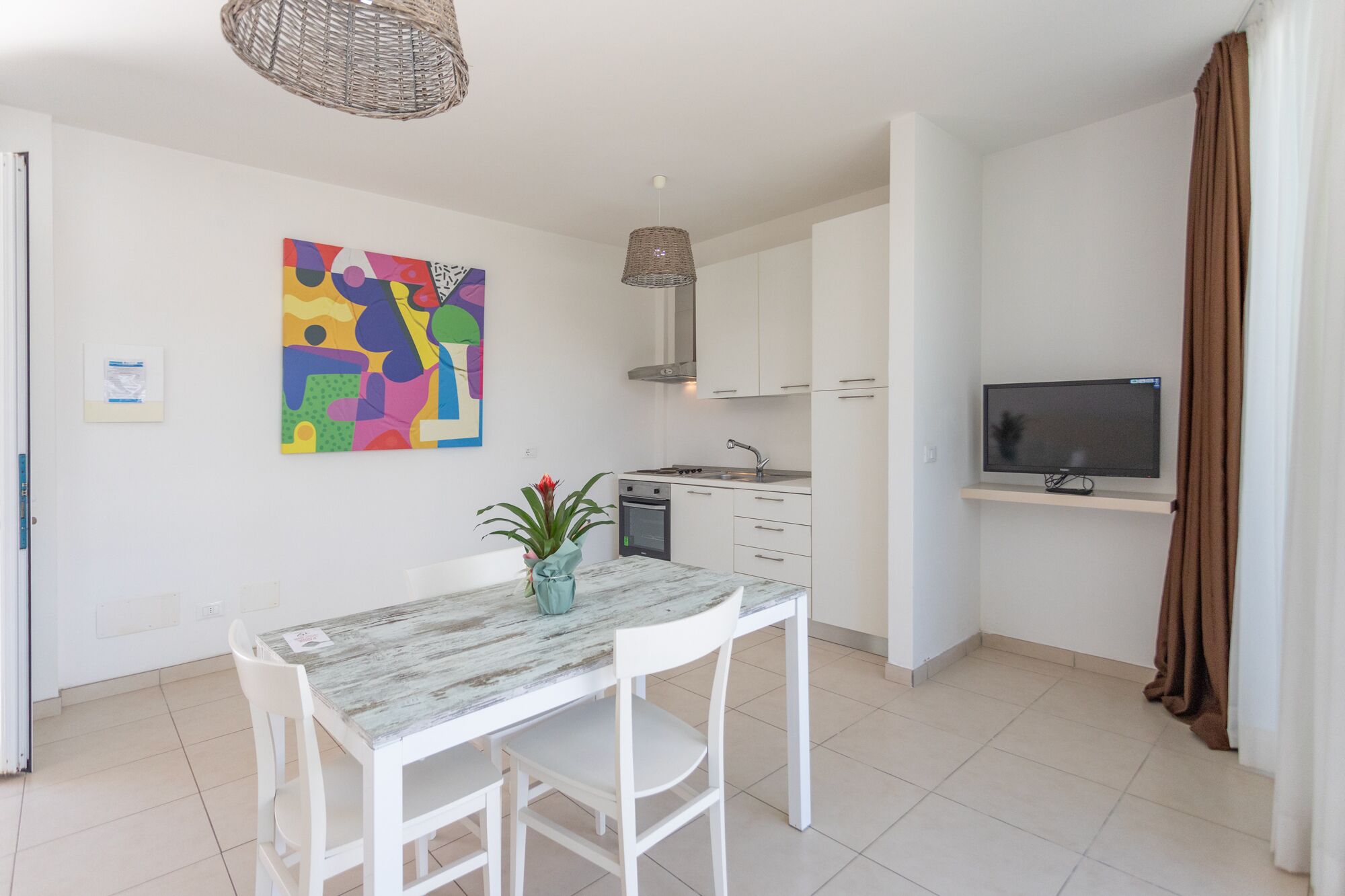 Une cuisine moderne avec des meubles blancs, une table à manger et un téléviseur fixé au mur.
