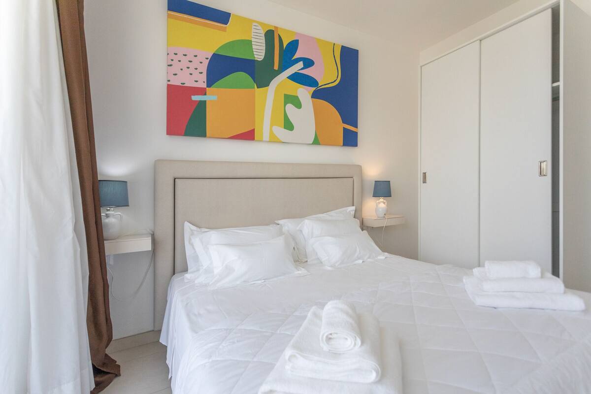 A hotel room with a bed, a nightstand, a lamp, a painting, and a wardrobe.