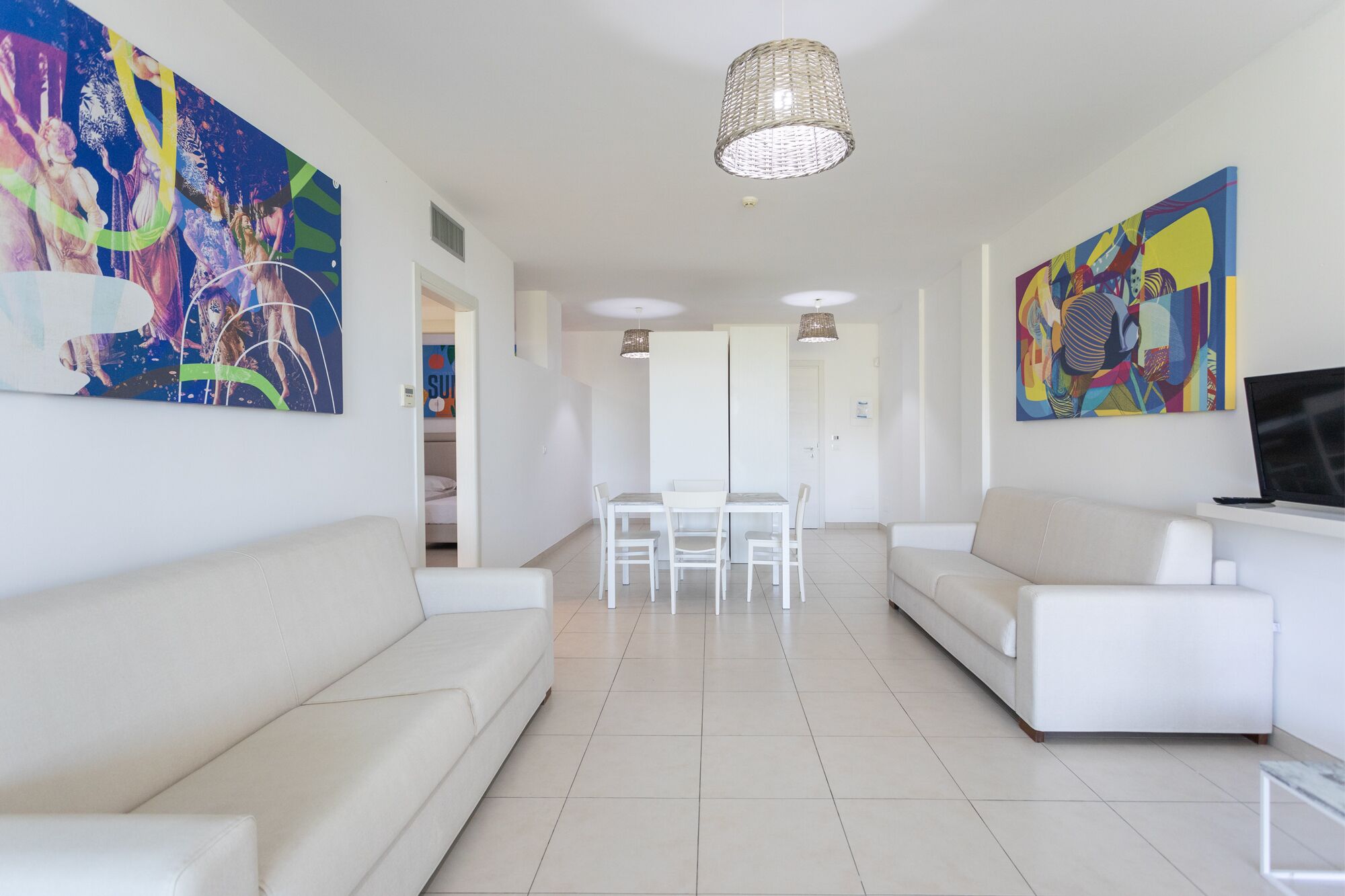 Ein modernes Wohnzimmer mit weißen Sofas, einem Esstisch und farbenfrohen abstrakten Gemälden.