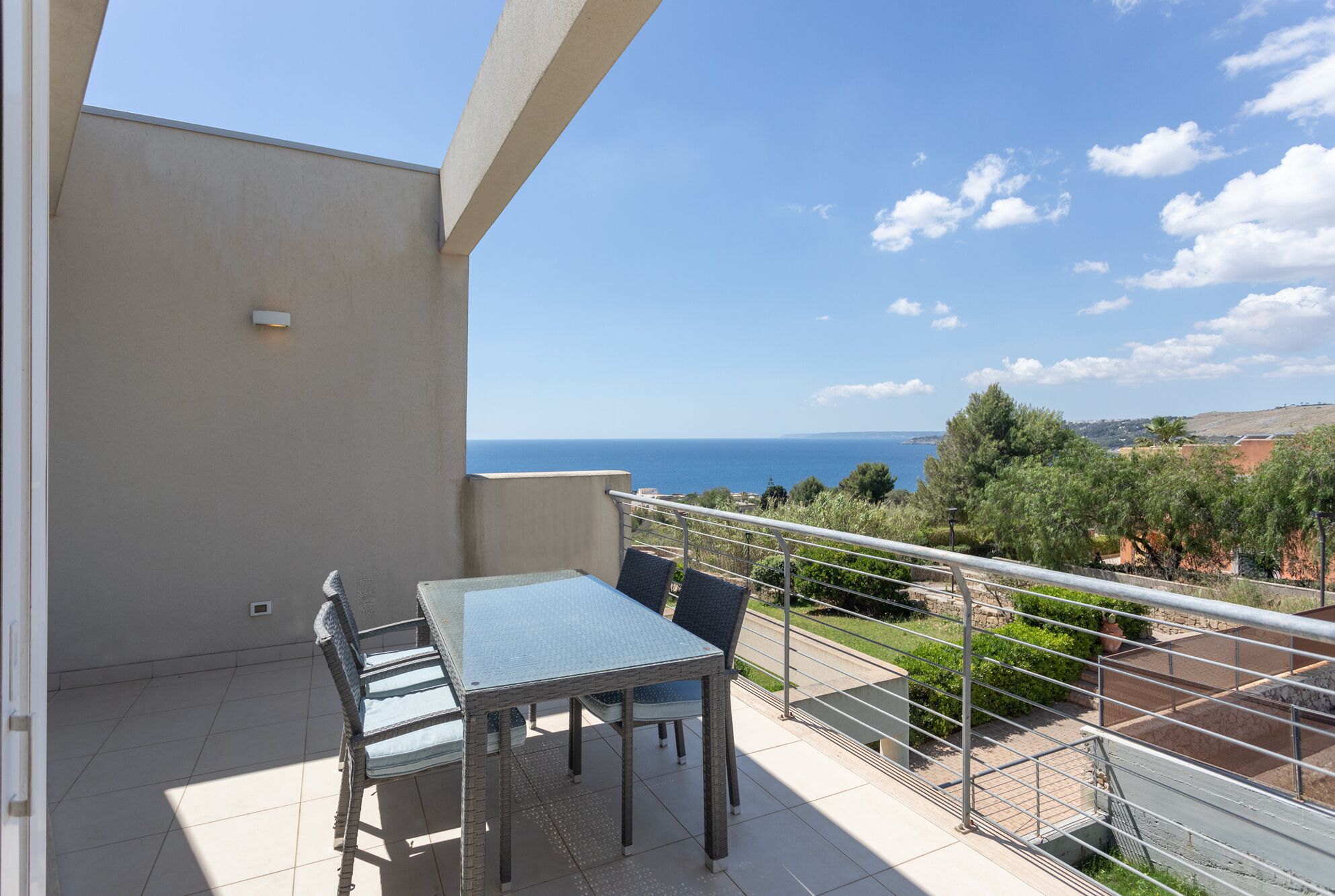 A balcony with a table and chairs, overlooking a coastal view.
