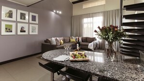 Een moderne woonkamer met een eethoek, met een ronde granieten tafel, een zithoek en een groot raam met gordijnen.