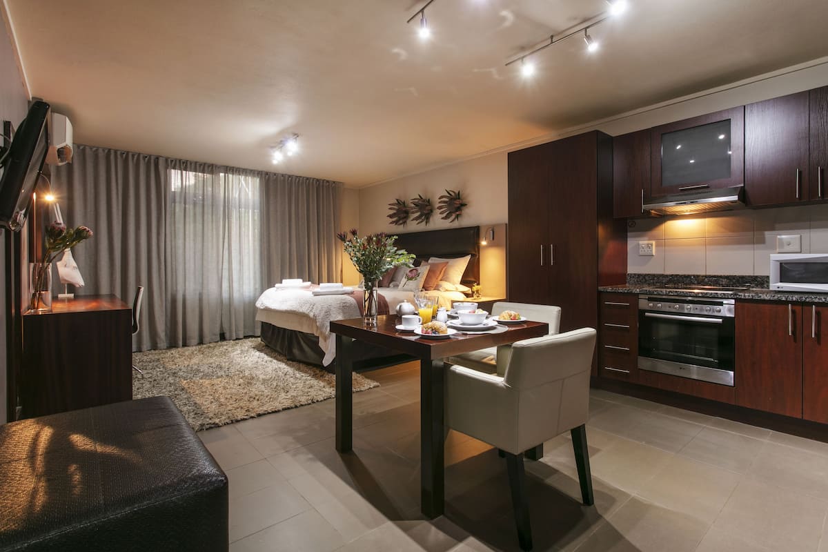A modern hotel room with a bed, bedside table, and a dining area with a table and chairs.
