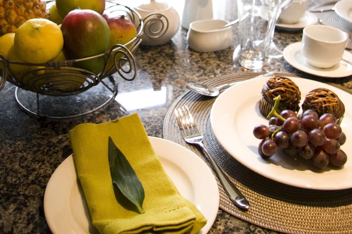 A dining table set with fruits, a pitcher, cups, and a plate with grapes.