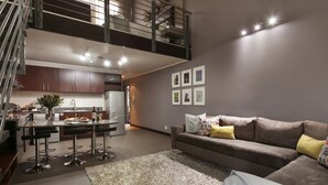Een moderne keuken met een eethoek, een trap naar een hoger niveau en een woonkamer met een bank en kussens.