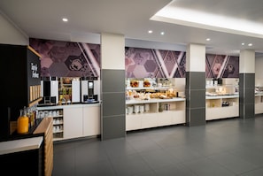 A modern hotel lobby with a coffee station, a fruit display, and a seating area.