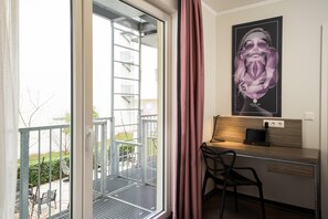 Una habitación de hotel con balcón, un escritorio con silla y un cartel en la pared.