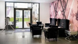 Een modern interieur met een glazen deur, zwarte beklede stoelen, een klein rond tafeltje en een muur met een groot abstract schilderij.