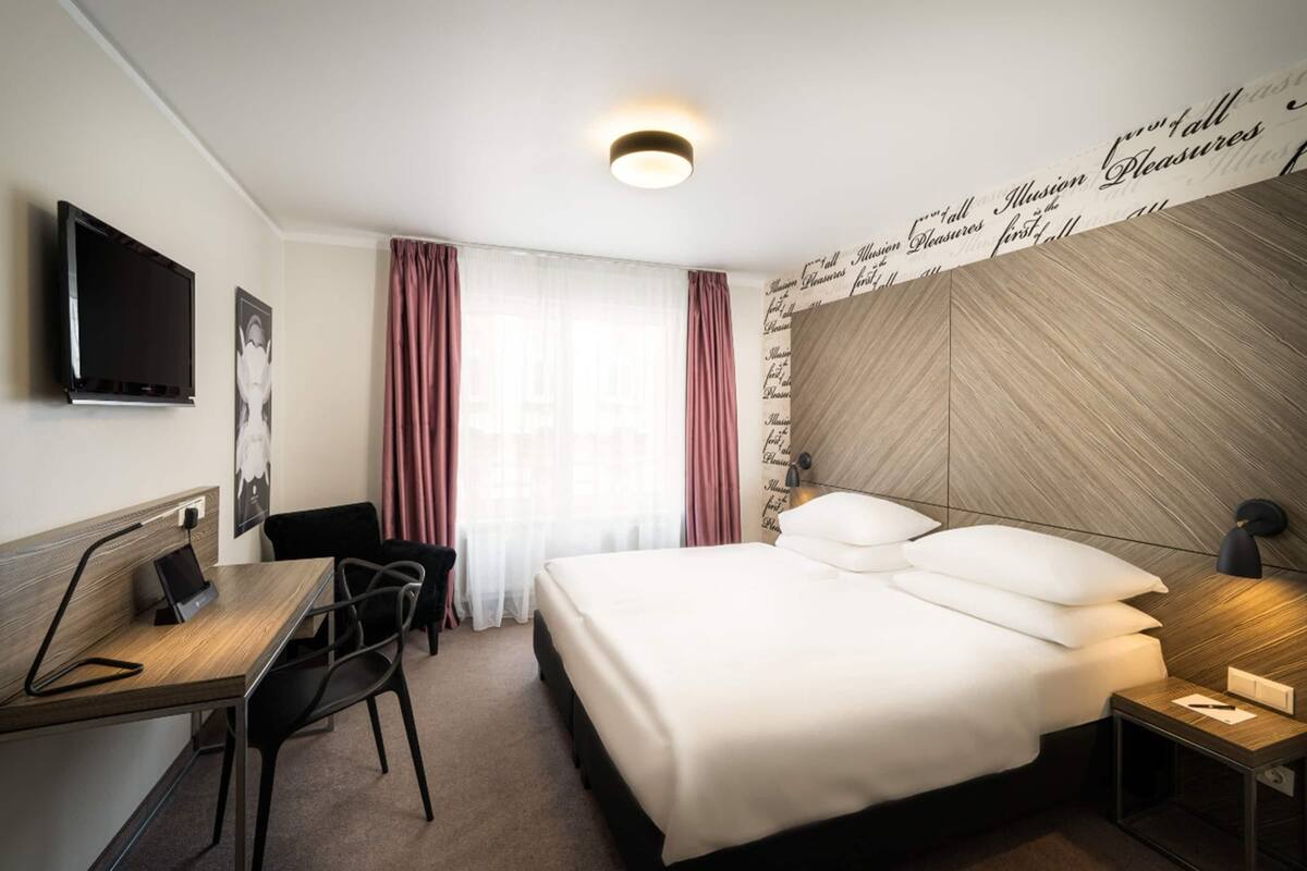 Une chambre d’hôtel comprenant un lit, un bureau avec une chaise, une télévision et une lampe fixée au mur.