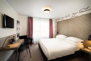 Ein Hotelzimmer mit einem Bett, einem Schreibtisch, einem Sessel, einem Fernseher und einer Wand mit einem Dekor.