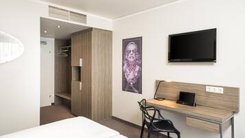 Una habitación de hotel con cama, escritorio, silla, televisor y armario.