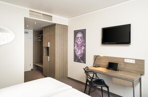 A hotel room with a bed, a desk with a chair, a TV, and a wardrobe.