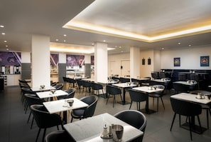 Ein modernes Restaurant mit mehreren Tischen, Stühlen, einer Küche und einer Bar.