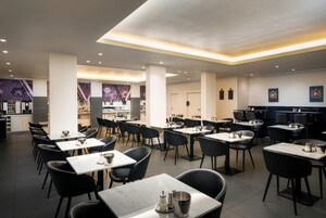Um restaurante moderno com várias mesas e cadeiras, uma área de cozinha e um bar.