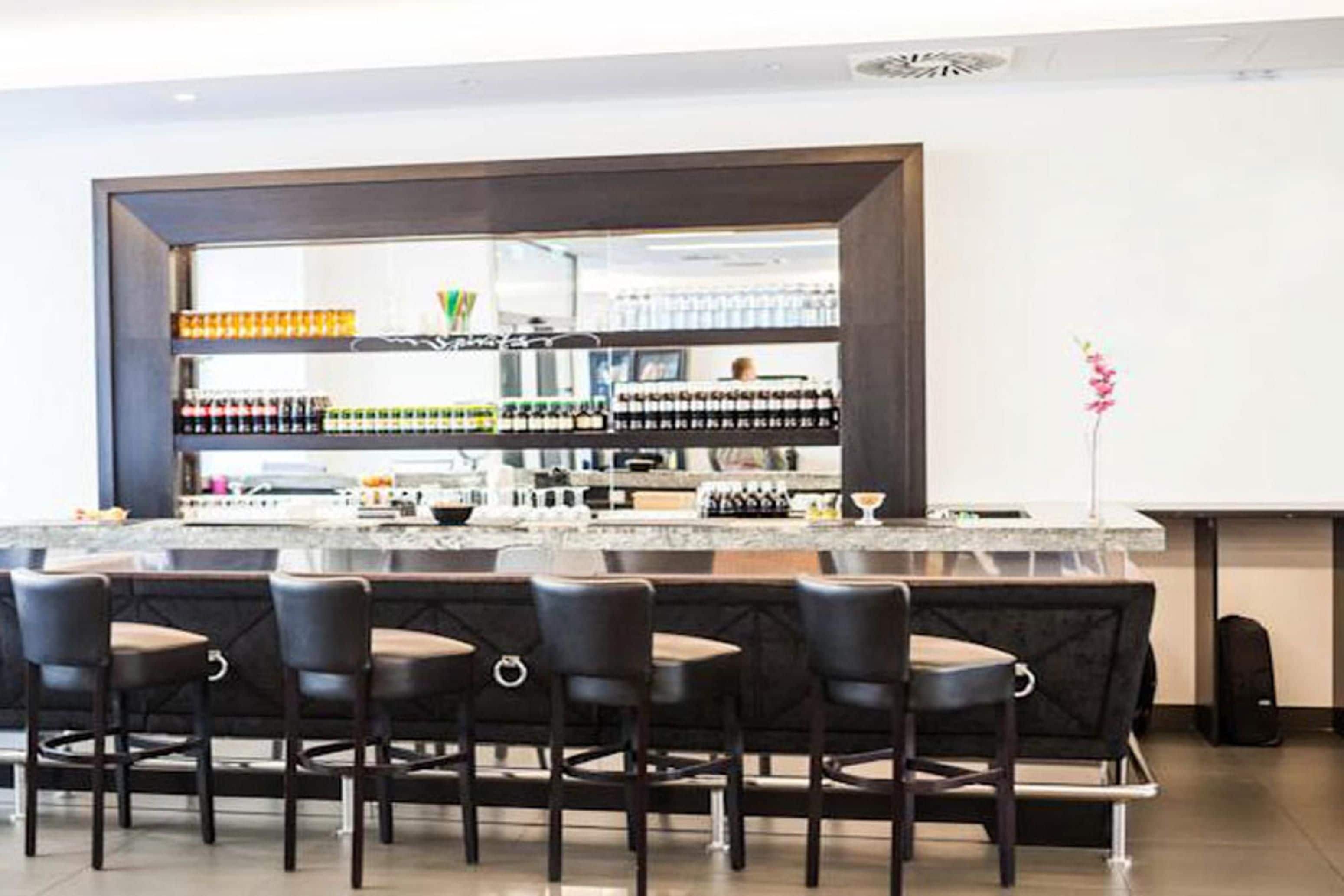 Una zona de bar con encimera de mármol, varias botellas y taburetes.