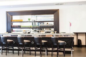 Eine Bar mit Marmorplatte, zahlreichen Flaschen und Barhocker.