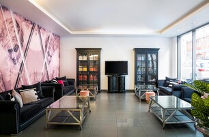 Uma sala de estar moderna com sofás pretos, mesas de centro de vidro e duas estantes repletas de livros.