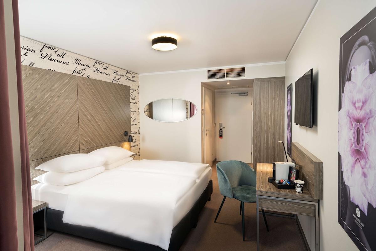 Une chambre d’hôtel comprenant un lit, un bureau avec une chaise, un miroir et un téléviseur.