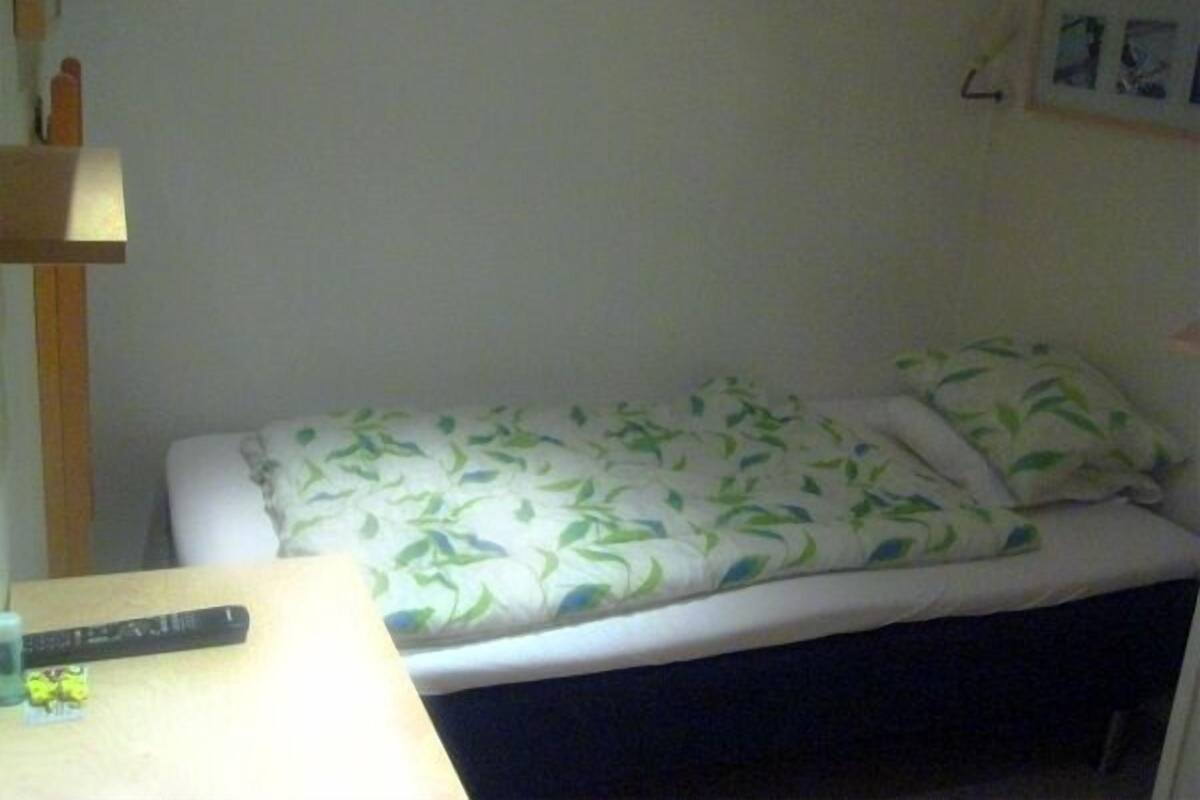 Une petite chambre avec un lit simple, une couvre-lit à motifs, une table de chevet avec une télécommande et un tableau accroché au mur.