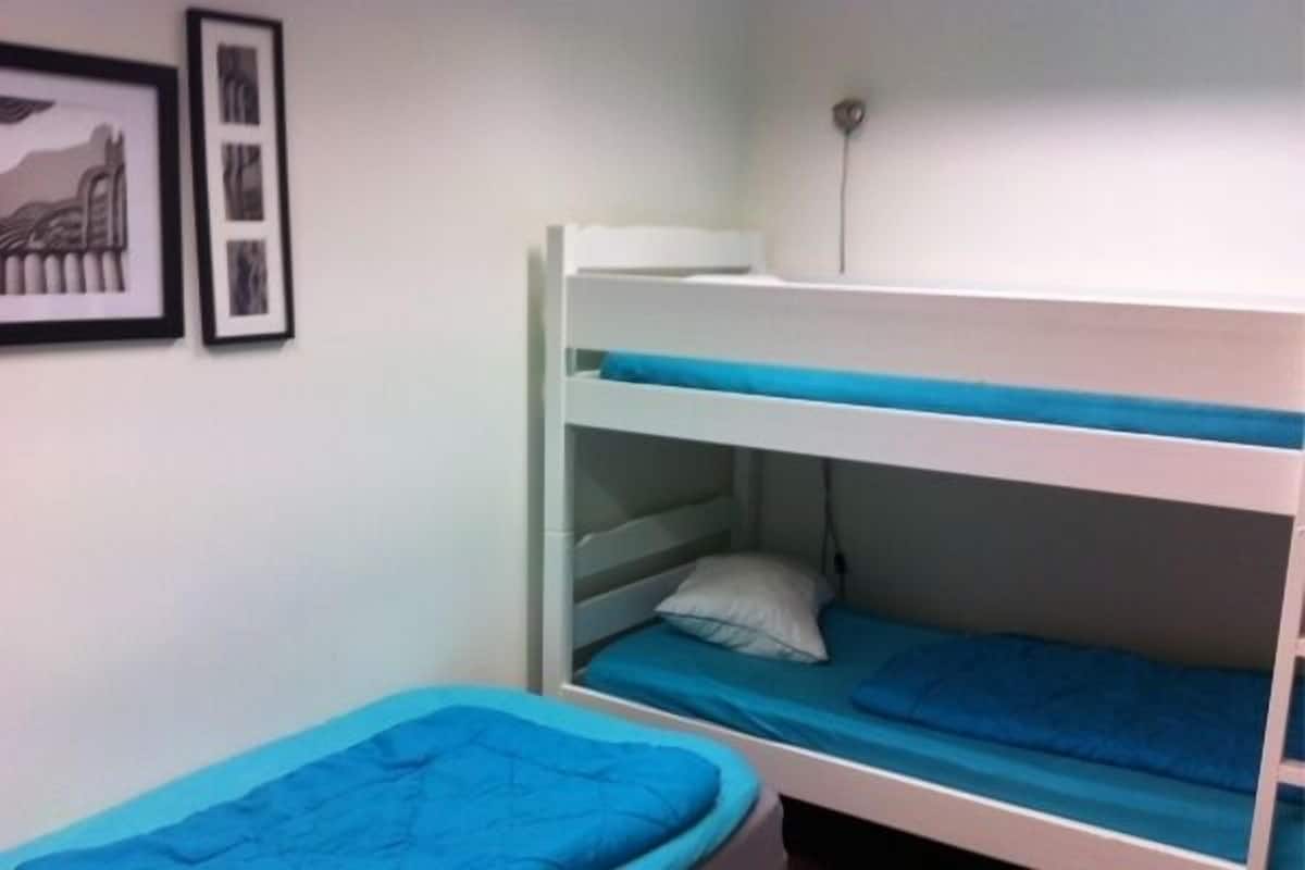 Une chambre avec un lit superposé, un mur blanc, un tableau encadré et un interrupteur.