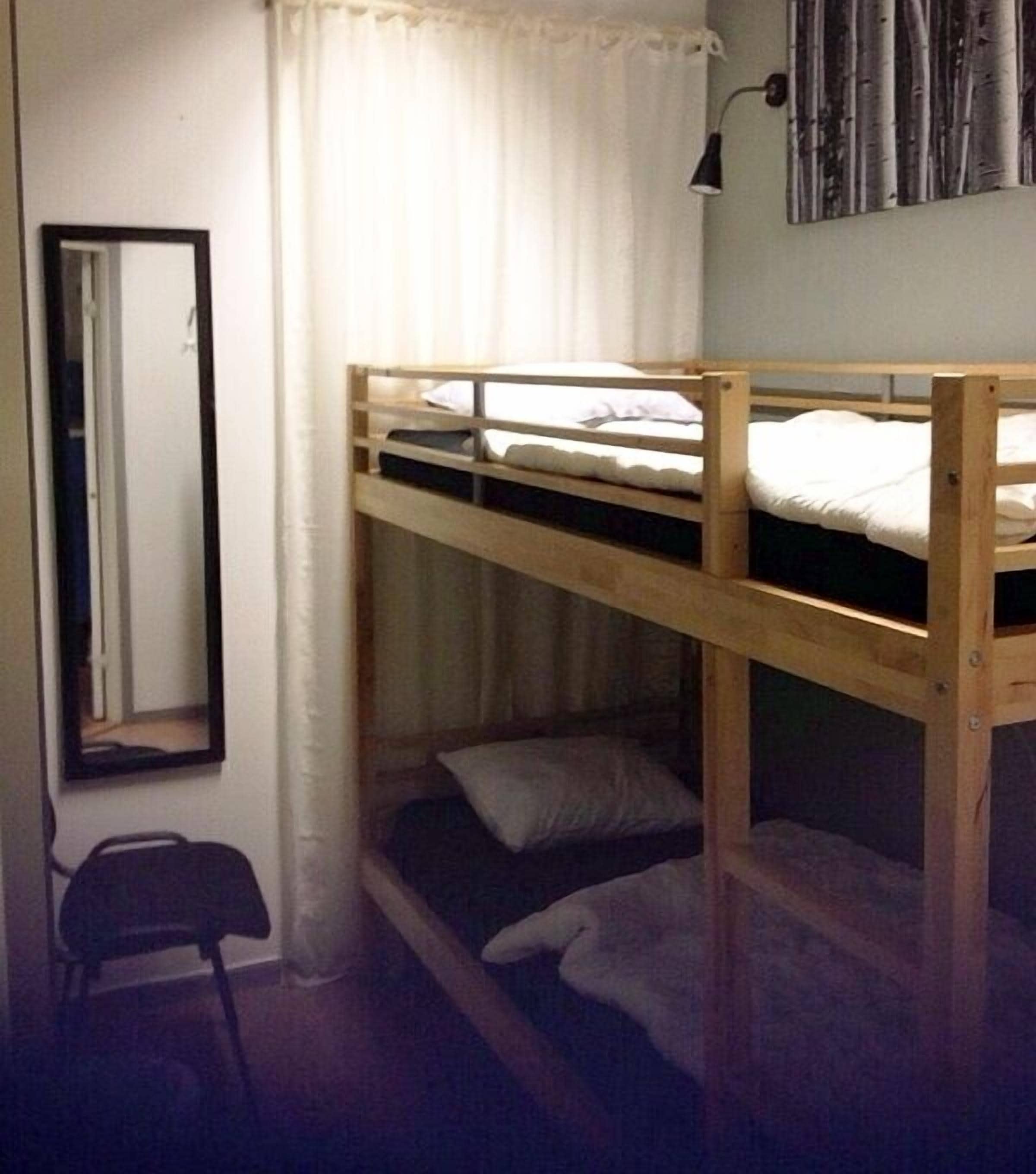 Habitación con literas, un espejo, una silla y una lámpara fijada a la pared.