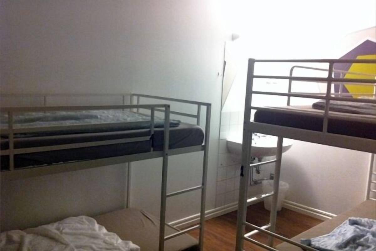 Une chambre avec un lit superposé, une fenêtre, un lavabo et une petite table de chevet.