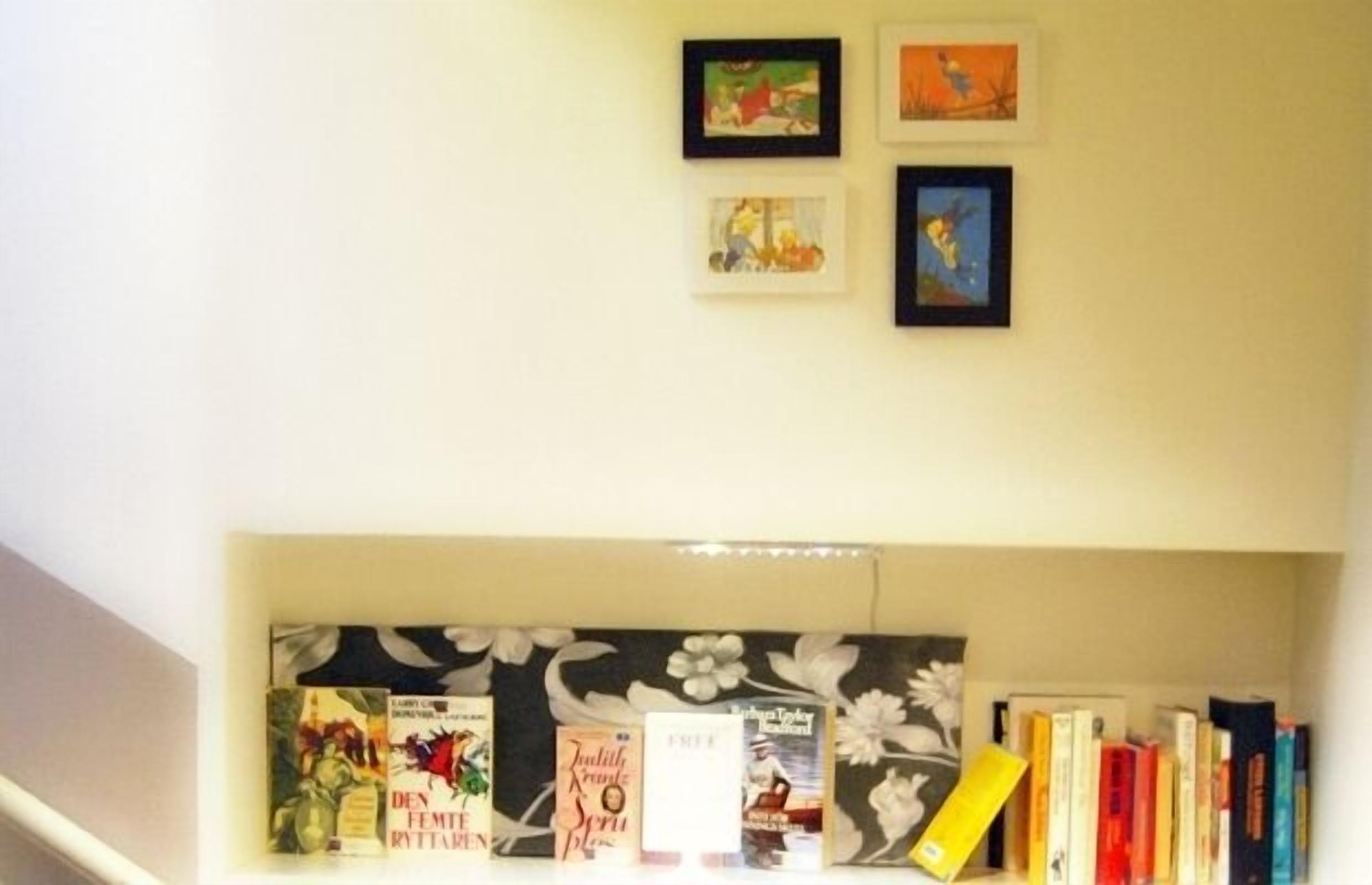 A bookshelf with books and framed pictures on a wall.