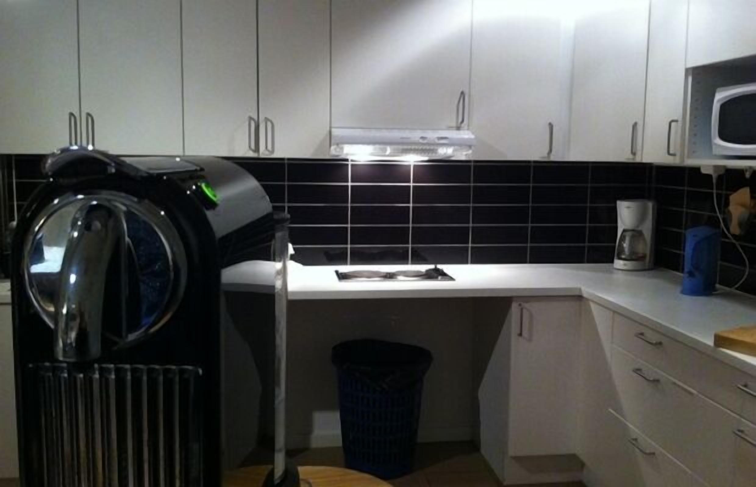 A compact kitchen with white cabinets, a black tiled backsplash, a microwave, and a coffee maker.