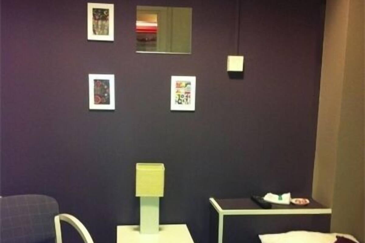 Une chambre à coucher comprenant un lit, une table de chevet, une chaise, une petite table et un mur orné de trois tableaux encadrés.